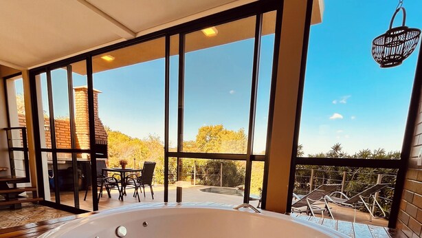 A large indoor hot tub with a view of a brick chimney and outdoor patio furniture through large windows. - Nativos de Minas (Santana do Riacho)