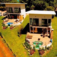 Una casa moderna de dos plantas con piscina, un porche cubierto y un césped cuidado.