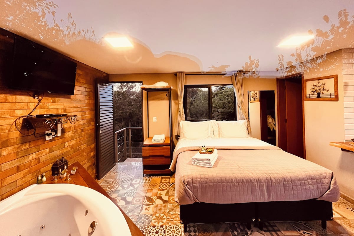 A bedroom with a large bed, a bathtub, and a TV mounted on the wall.