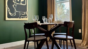 Un coin repas avec une table dressée pour quatre personnes, un luminaire suspendu et un grand tableau abstrait accroché au mur.