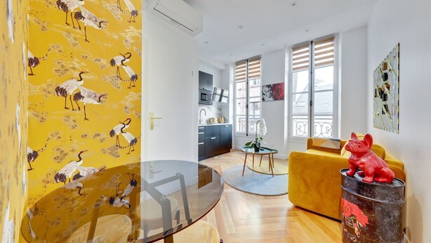 Un espace de vie moderne avec un mur jaune, une table en verre, un canapé jaune et une sculpture rouge.
