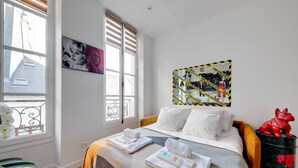 Une chambre d’hôtel avec un lit, une fenêtre, un tableau et une statue rouge.
