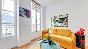Un salon avec un canapé jaune, une table basse en verre et une plante en pot.