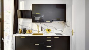 A modern kitchen with black cabinets, a marble countertop, a gold faucet, a microwave, a toaster, and a coffee maker.