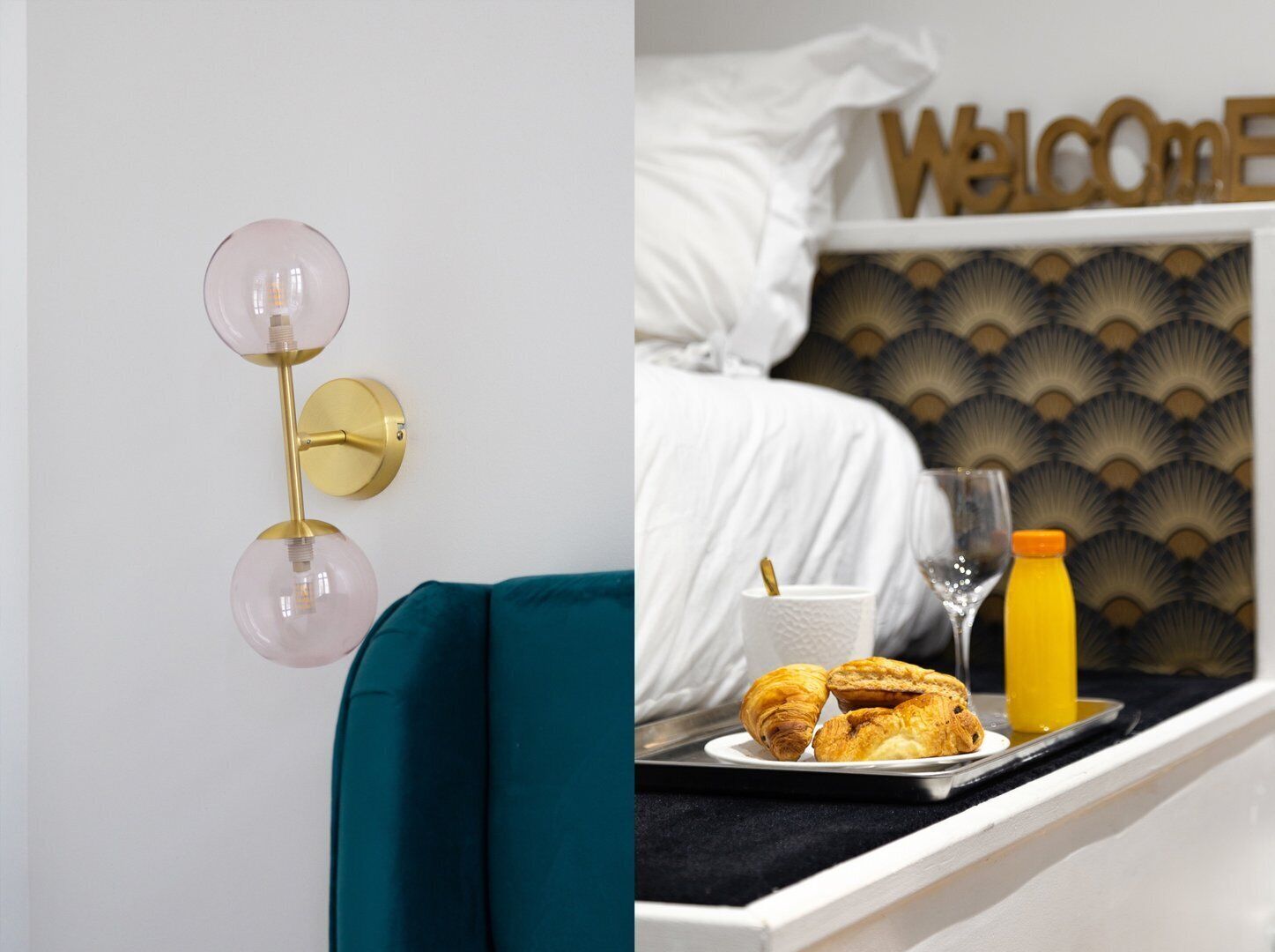 A modern room with a teal sofa, a wall-mounted light fixture, a bed with a 'Welcome' sign, and a tray with croissants and juice.