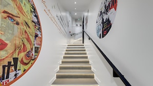 A modern staircase with a handrail, surrounded by walls adorned with various posters and artwork.