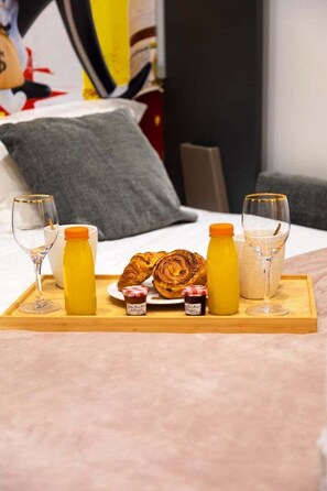 Ett frukostbricka med croissanter, juice, sylt och ett glas mjölk, placerat på sängen.