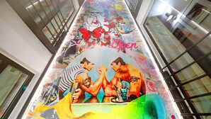 Un largo pasillo con un mural colorido que muestra dos figuras en un ring de boxeo, rodeado de grafitis vibrantes y motivos florales.