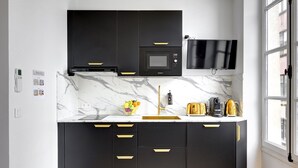 Una cocina moderna con armarios negros, encimera de mármol y microondas integrado.