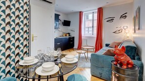 Un salon moderne avec un coin repas, une cuisine à l’arrière-plan et une statue de renard rouge posée sur un conteneur en métal.