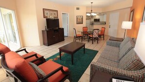 A living room with a sofa, chairs, a coffee table, a television, and a dining area with chairs and a table. - Vacation Village Reservations (Kissimmee)