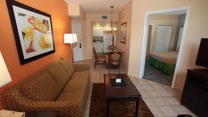 A living room with a patterned sofa, a dining table, and chairs. There is a kitchen area visible in the background. - Vacation Village Reservations (Kissimmee)