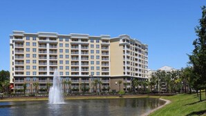A multi-story hotel with balconies, a fountain, and a grassy area with trees. - Vacation Village Reservations (Kissimmee)