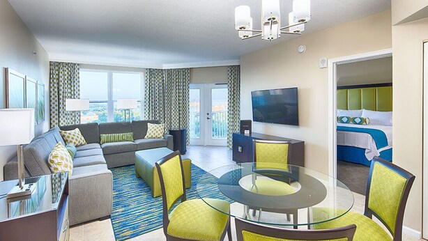 A modern hotel room with a living area, a dining table, and a balcony with a view. - Vacation Village Reservations (Kissimmee)