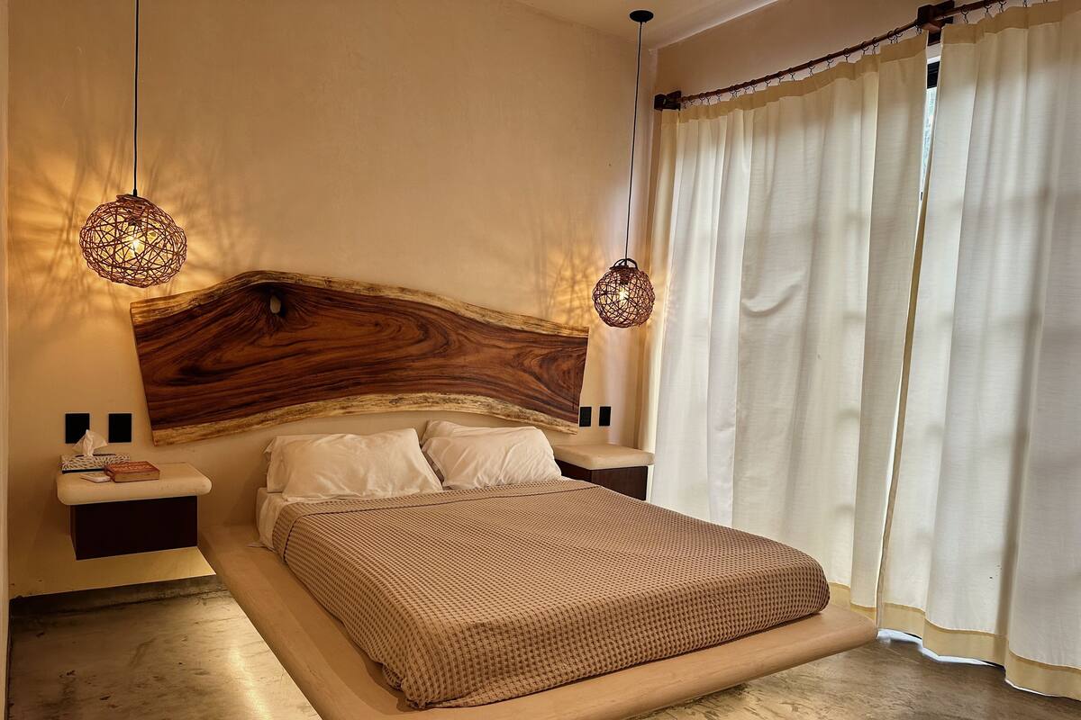 A bedroom with a wooden headboard, two bedside tables, a bed with a brown checkered bedspread, and two hanging spherical light fixtures.