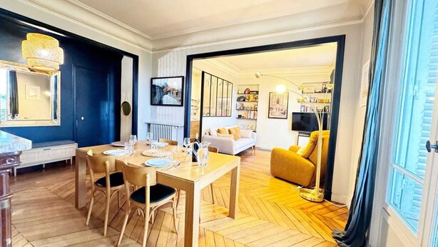 Un coin repas avec une table en bois dressée pour quatre personnes, un canapé et une lampe sur pied.