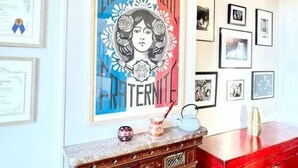 Une pièce comprenant un meuble en bois d’époque, une commode rouge et un mur décoré d’images encadrées et d’une affiche.