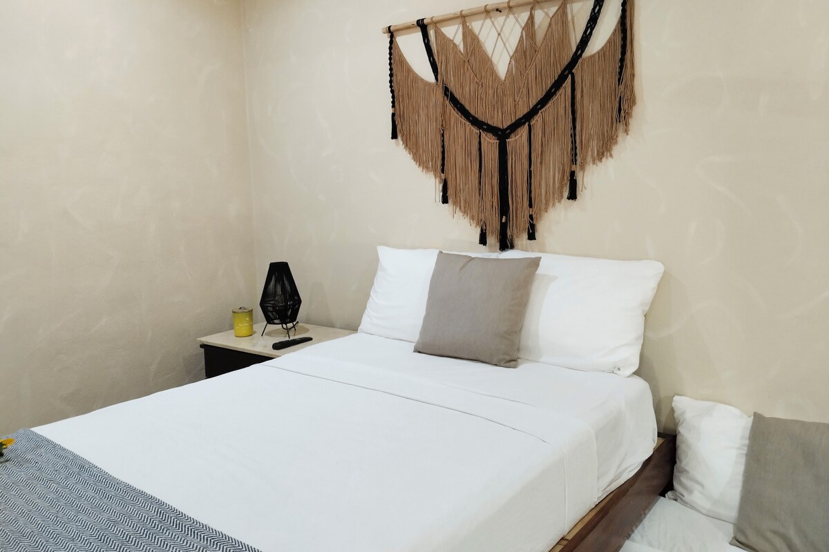 A hotel room with a bed, a bedside table, a lamp, and a wall hanging.