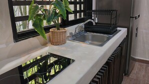 Una cocina con un lavamanos de acero inoxidable, un grifo negro, una cesta tejida con una planta y un refrigerador de acero inoxidable.