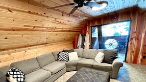 Ein gemütliches Zimmer mit einem Ecksofa, einem Deckenventilator und einem großen Fenster.