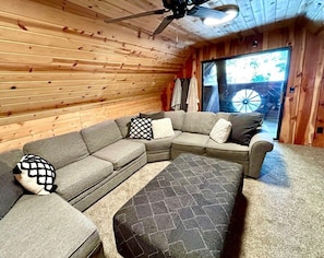 A cozy room with a sectional sofa, a ceiling fan, and a large window.