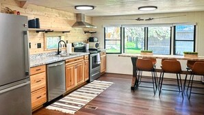 Eine moderne Küche mit Holzausstattung, Edelstahlgeräten, einem großen Fenster und einem Essbereich mit Stühlen.