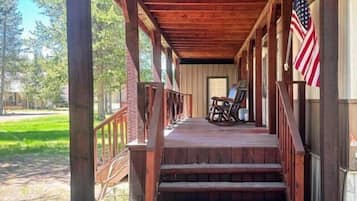 A wooden porch with steps leading to a door, an American flag, and a view of a grassy area.