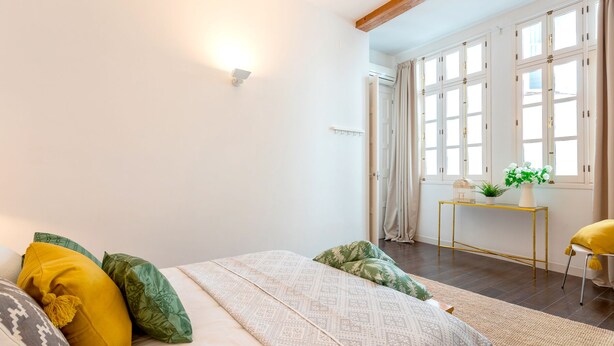 A bedroom with a bed, pillows, a bedside table with a plant, and a window with curtains. - 3 Bd Apartment With Balconies Next to Larios Street Larios (Málaga)