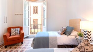 A hotel room with a bed, a chair, a bedside table with a lamp, and a view of the outside balcony. - 3 Bd Apartment With Balconies Next to Larios Street Larios (Málaga)