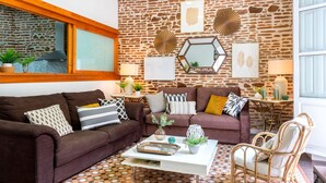 A living room with a stone wall, two sofas, a coffee table, and wicker chairs. - 3 Bd Apartment With Balconies Next to Larios Street Larios (Málaga)