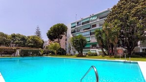 A swimming pool with a metal ladder, surrounded by greenery and a multi-story building with balconies. - 2 Bedroom With Private Terrace and Communal Pool in Marbella Center Ricardo Soriano Terrace (Marbella)