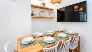 A dining area with a wooden table set for six, white chairs, and a TV mounted on the wall. - Amazing Apartment 5 Bd in the Heart of Granada Alh Ndiga (Granada)