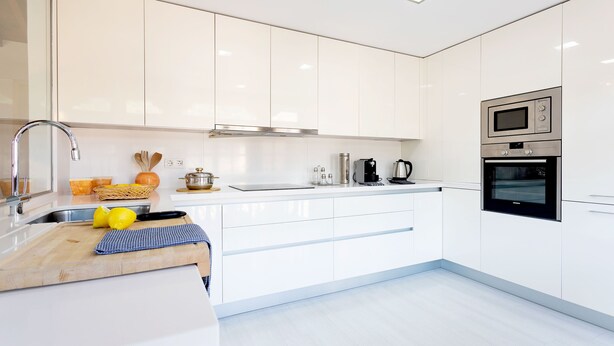 Eine moderne Küche mit weißen Schränken, einer Edelstahl-Spüle, einer Holz Arbeitsplatte und eingebauten Geräten, darunter eine Mikrowelle und ein Backofen.