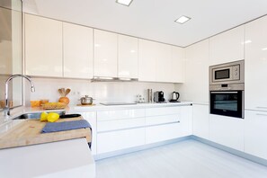 Een moderne keuken met witte kasten, een roestvrijstalen spoelbak, een houten werkblad en geïntegreerde apparatuur, waaronder een magnetron en oven.
