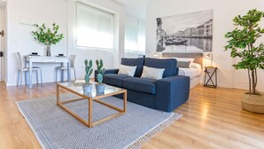 Ein modernes Wohnzimmer mit einem blauen Sofa, einem Couchtisch und einem Essbereich mit einem weißen Tisch und Stühlen.