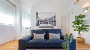 Ein modernes Wohnzimmer mit einem blauen Sofa, einer Kakteenpflanze, einem Glastisch und einem an der Wand hängenden Gemälde, das eine Kanalansicht zeigt.