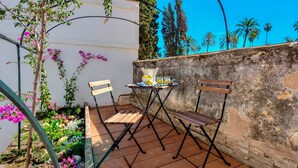 An outdoor seating area with two wooden chairs and a small table, surrounded by a garden with various plants and flowers. - Beautiful 4 Bd House With Terrace Views to the Alcazar Gardens Casa Alcazar (Seville)