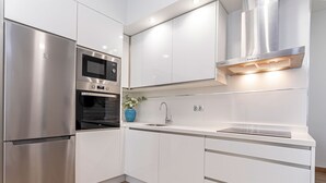 Cozinha moderna com eletrodomésticos de aço inoxidável, armários brancos e forno embutido.