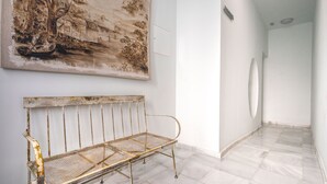 Uma galeria com uma grande pintura de paisagem, um banco de metal e um chão de azulejos brancos.