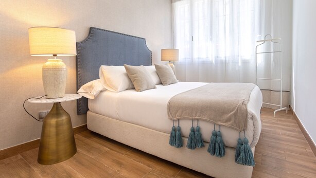 Quarto de hotel bem arrumado com uma cama, duas mesas de cabeceira, uma luminária e um guarda-roupa.