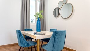 Uma sala de jantar com uma mesa de madeira, quatro cadeiras de veludo azul, um vaso azul com plantas verdes e três espelhos redondos na parede.
