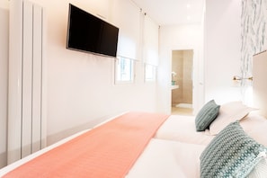 A modern hotel room with a large bed, a flat-screen TV mounted on the wall, and a view of the bathroom.