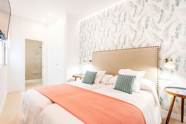 A hotel room with a large bed, two bedside tables, a headboard with a leaf pattern, and a door leading to a bathroom.