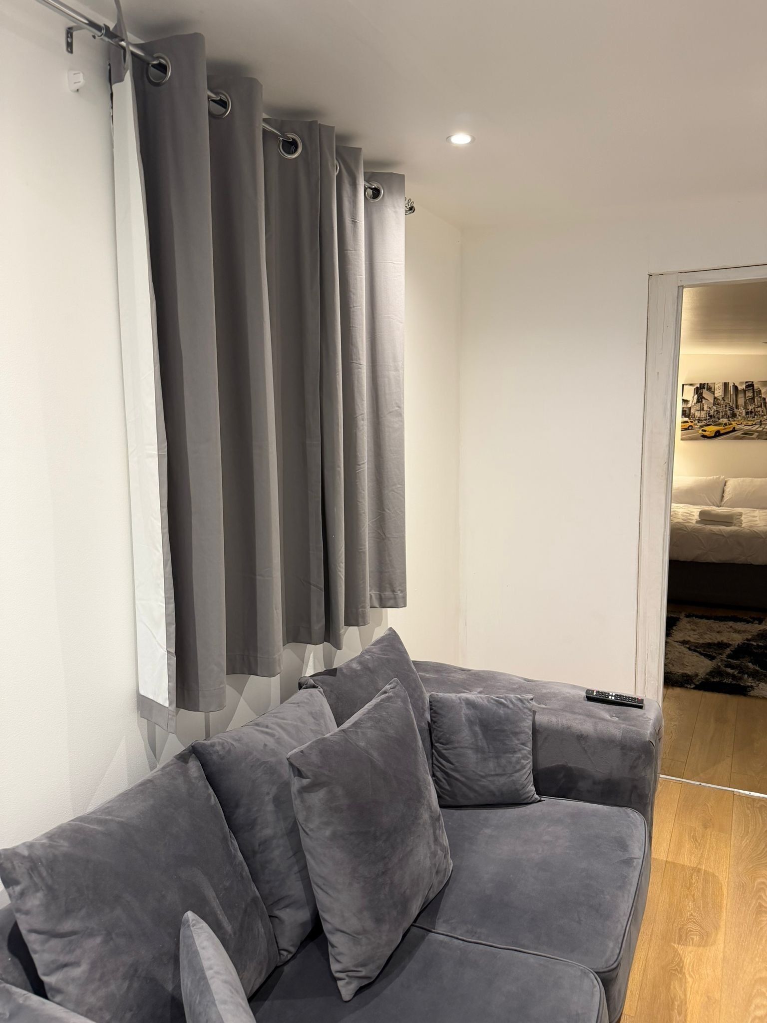 Ein modernes Wohnzimmer mit einem grauen Sofa, passenden Kissen, einem Vorhang und einer Fernbedienung auf dem Sofa.