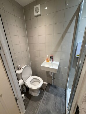 A small, modern bathroom with a toilet, a sink, and a shower. - 
Cozy Retreat | Free Parking & Patio with Smart TVs (Romford)