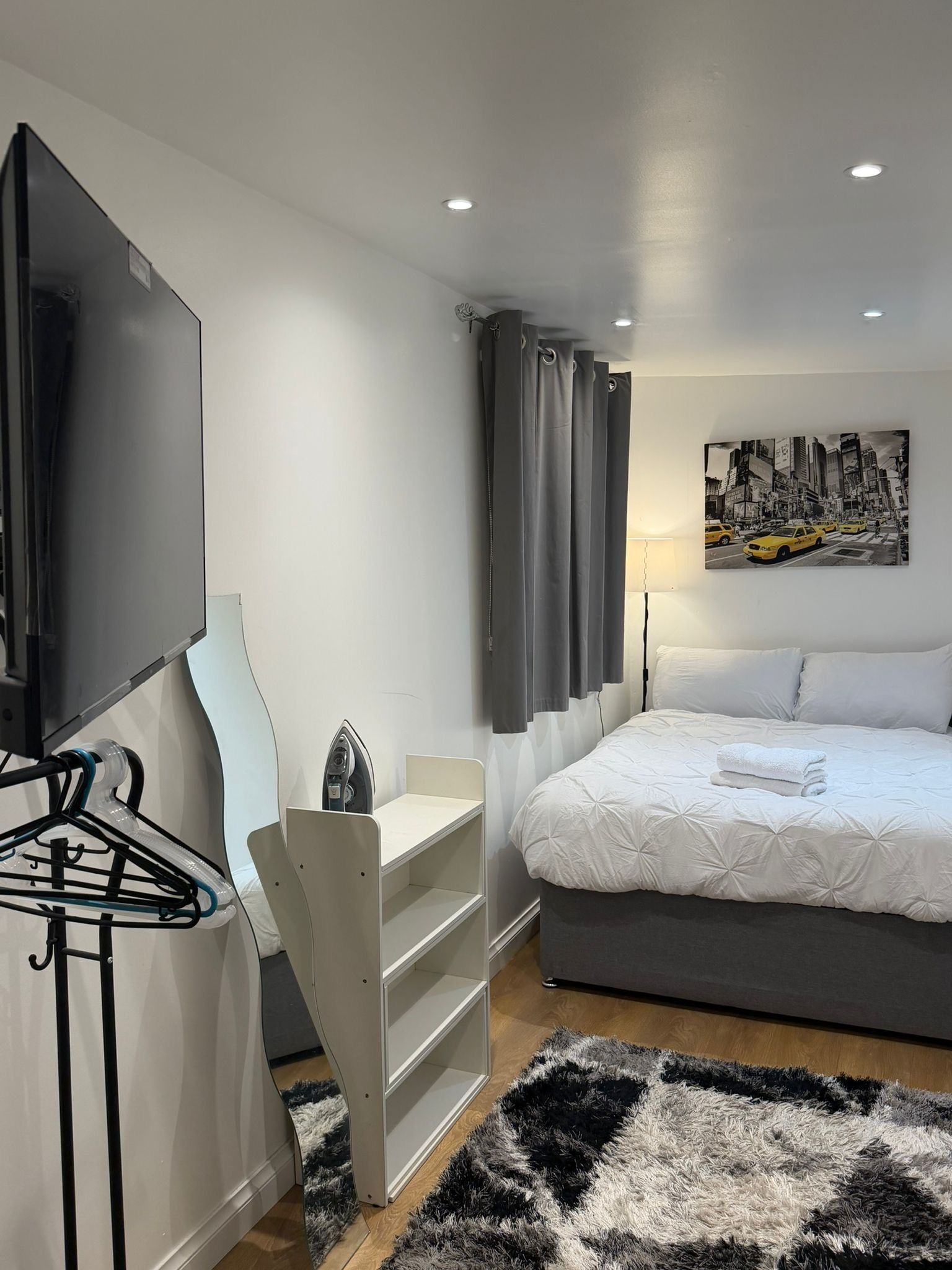 Ett modernt hotellrum med en säng, en platt-TV, ett skrivbord och en tavla som föreställer en stadsbild.
