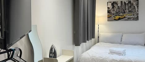 A modern hotel room with a bed, a flat-screen TV, a desk, and a cityscape painting.