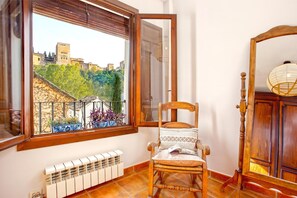 Una stanza con una sedia di legno, un termosifone, una finestra vista castello e uno specchio.