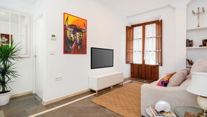 Una sala de estar con una televisión de pantalla plana, un cuadro, un sofá, una mesa de centro de vidrio y una planta en maceta.