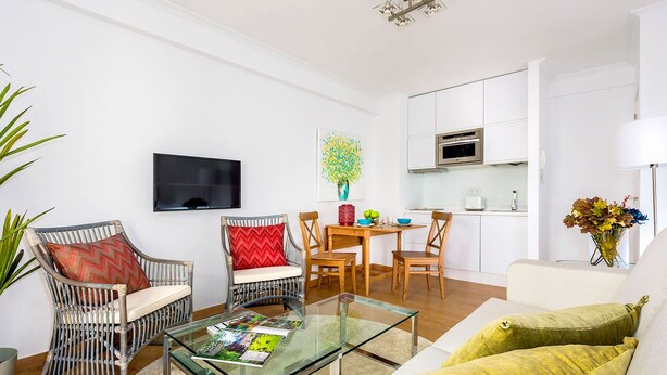 Un salon moderne avec une table basse en verre, des fauteuils en osier, un canapé et un coin repas comprenant une table et des chaises.